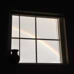 Picture of dark room with bright window and rainbow is seen out window