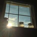 Picture of a window with the sun peeping through and jars sitting on the window